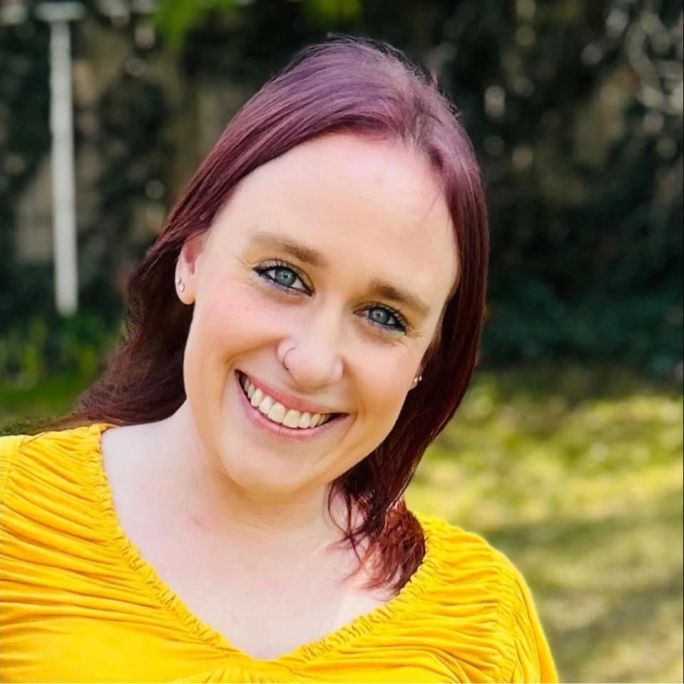 A smiling woman in a yellow top, photographed outdoors